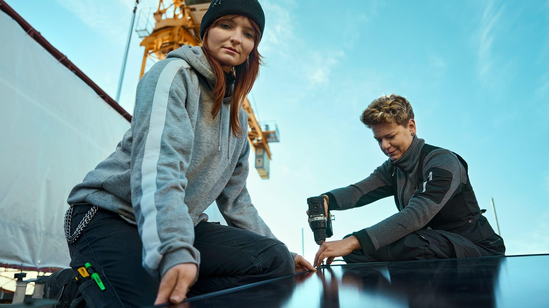 Zwei Dachdeckerinnen montieren ein Solarpanel auf einem Dach